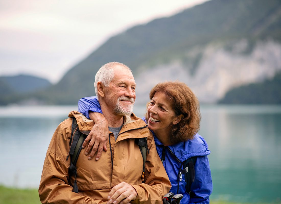 Medicare - Senior Pensioner Couple Hiking by Lake in Nature and Resting